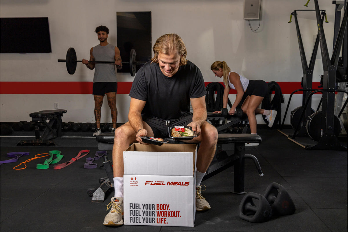 Man unboxing Fuel Meals at a gym, with people working out in the background.